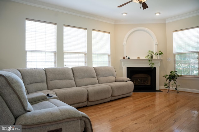 living area with a ceiling fan, baseboards, a fireplace with flush hearth, crown molding, and light wood-type flooring