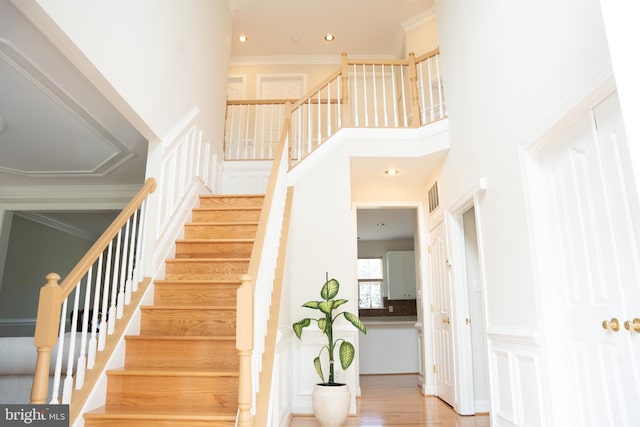 stairs featuring visible vents, wood finished floors, recessed lighting, a high ceiling, and crown molding