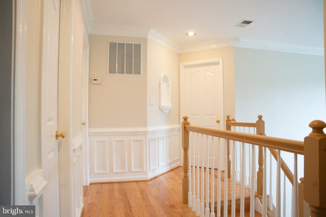 hall with wood finished floors, a wainscoted wall, visible vents, ornamental molding, and an upstairs landing