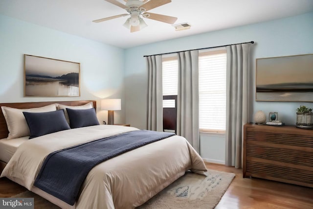 bedroom with ceiling fan, visible vents, multiple windows, and wood finished floors