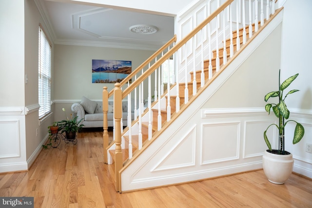 stairway featuring a decorative wall, wainscoting, crown molding, and wood finished floors