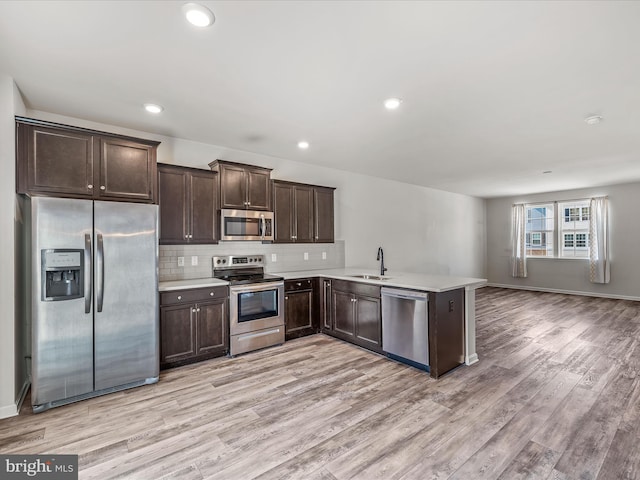 kitchen featuring dark brown cabinetry, stainless steel appliances, light countertops, light wood-type flooring, and backsplash