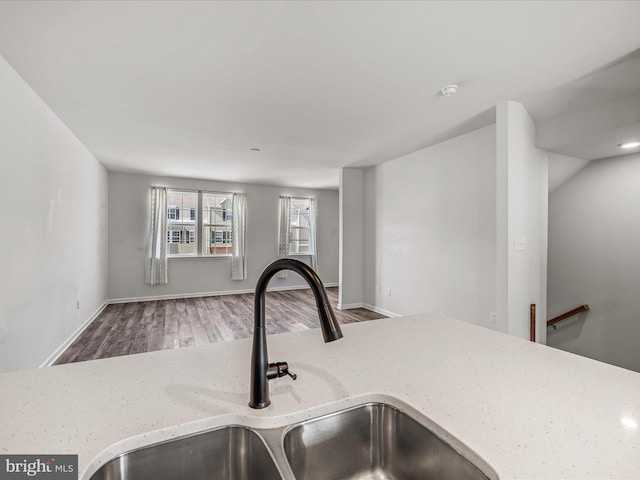 interior details featuring wood finished floors, a sink, light stone counters, and baseboards