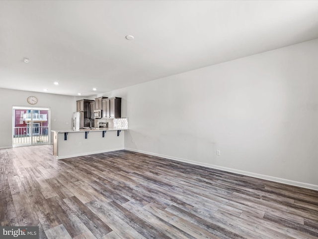 unfurnished living room with a sink, baseboards, wood finished floors, and recessed lighting