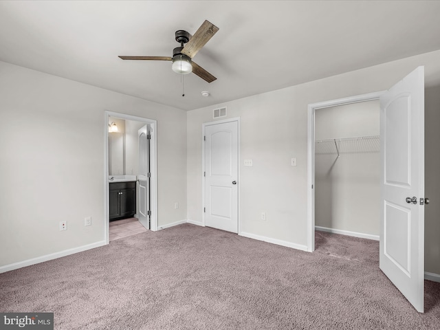 unfurnished bedroom featuring a closet, light colored carpet, a spacious closet, ensuite bath, and baseboards