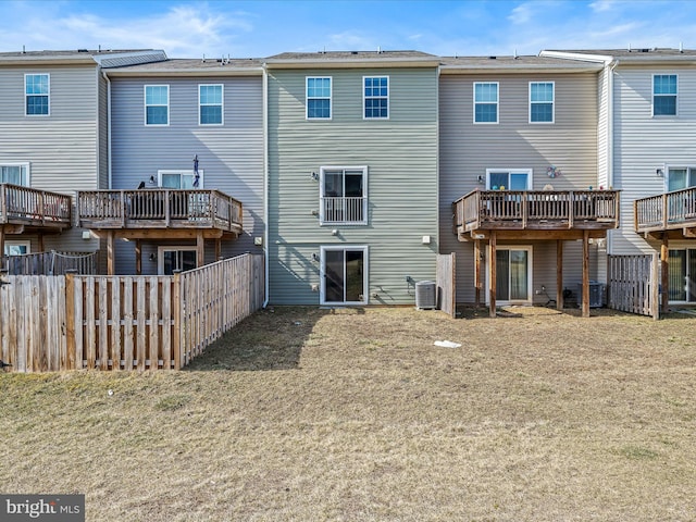 rear view of house with central AC, fence, and a lawn