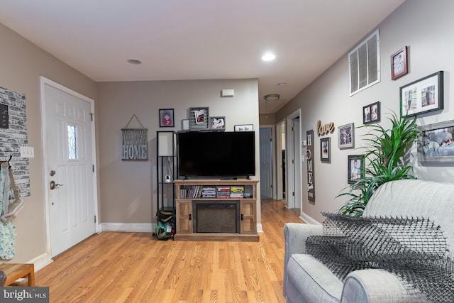 living area featuring light wood-style flooring, a fireplace, visible vents, and baseboards