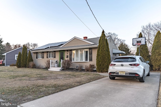 view of front of house with a shingled roof, roof mounted solar panels, a chimney, and a front yard