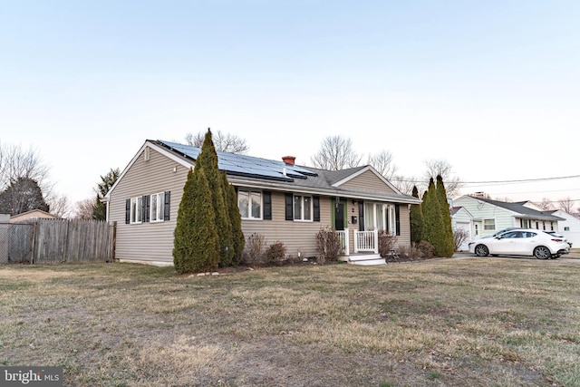 ranch-style home featuring roof mounted solar panels, fence, a chimney, and a front lawn