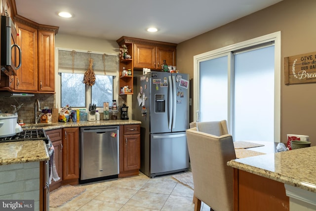 kitchen with brown cabinets, light stone countertops, stainless steel appliances, and a sink