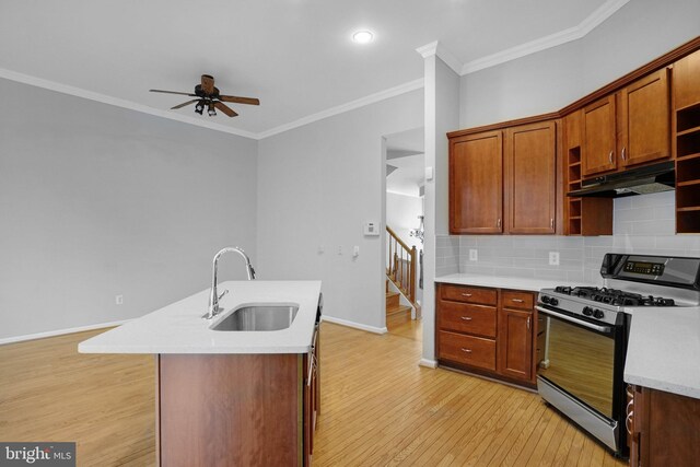 kitchen featuring tasteful backsplash, ceiling fan, under cabinet range hood, gas range oven, and a sink