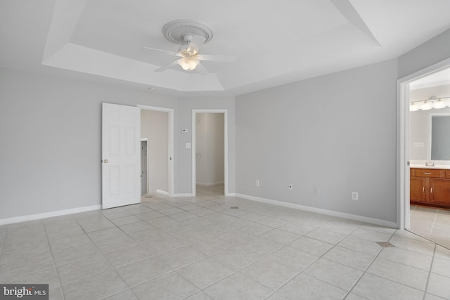 unfurnished bedroom featuring light tile patterned floors, baseboards, a tray ceiling, and a sink