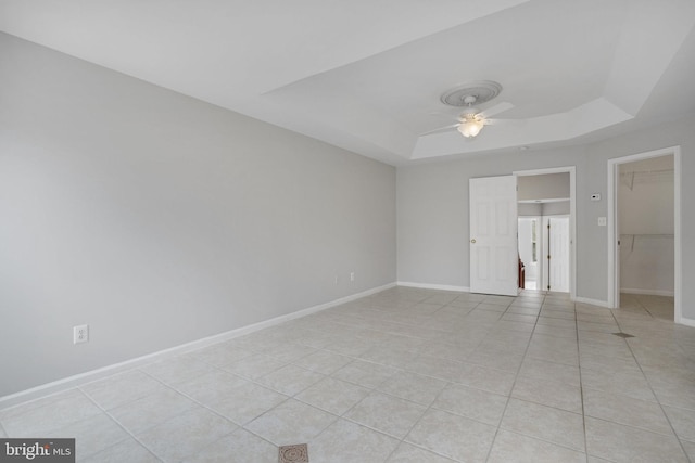 interior space featuring light tile patterned floors, a tray ceiling, baseboards, and a ceiling fan