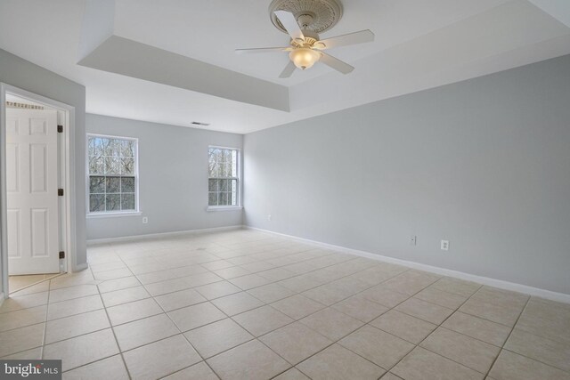 empty room with baseboards, light tile patterned floors, a ceiling fan, and a tray ceiling
