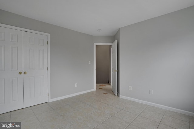 unfurnished bedroom featuring a closet, light tile patterned floors, and baseboards