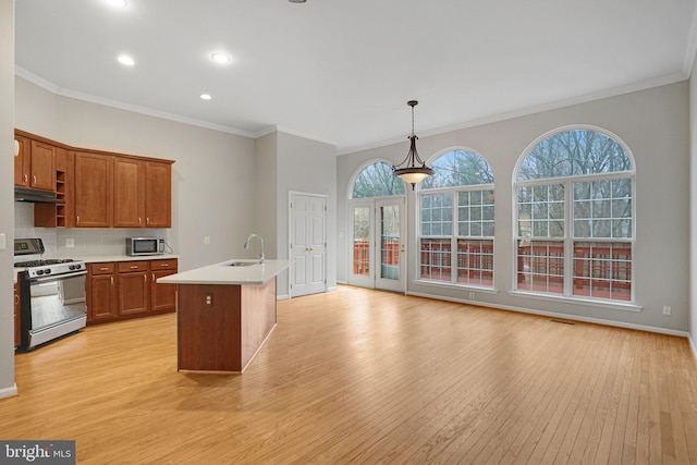 kitchen with gas stove, light wood-type flooring, a sink, under cabinet range hood, and tasteful backsplash