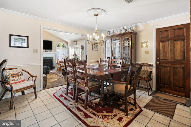 dining area featuring crown molding, a fireplace, light tile patterned floors, lofted ceiling, and an inviting chandelier