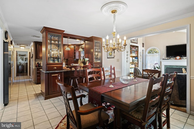 dining area featuring light tile patterned floors, a chandelier, a fireplace, visible vents, and crown molding