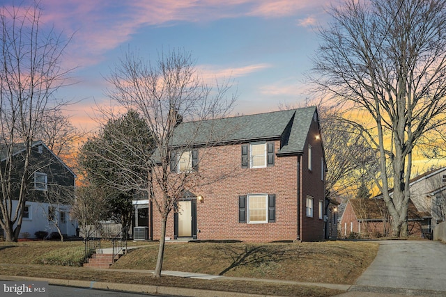 view of front of property featuring brick siding and roof with shingles