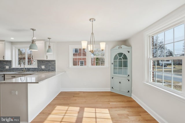 kitchen with tasteful backsplash, baseboards, white cabinets, light wood-type flooring, and a sink