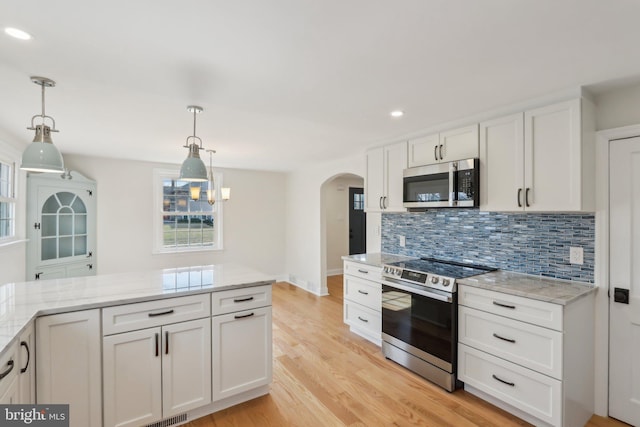 kitchen with arched walkways, stainless steel appliances, decorative backsplash, light wood-style floors, and white cabinetry