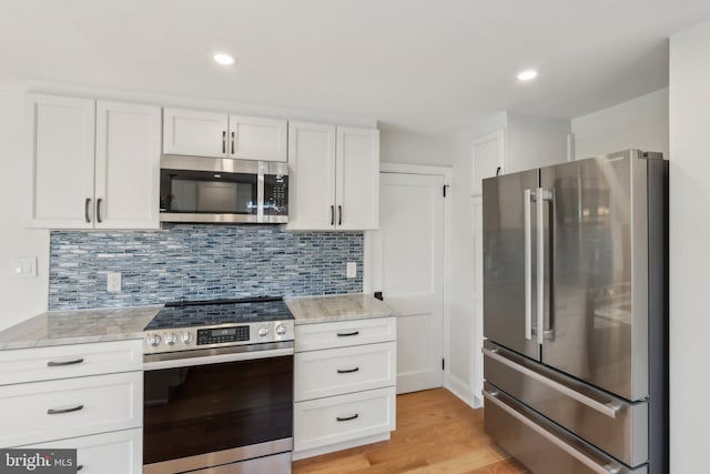 kitchen with tasteful backsplash, recessed lighting, appliances with stainless steel finishes, white cabinets, and light wood-type flooring