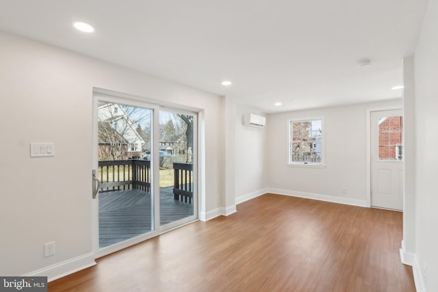 unfurnished room with a wealth of natural light, an AC wall unit, baseboards, and wood finished floors