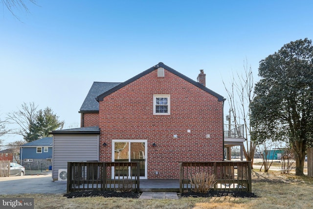 rear view of house with brick siding, a chimney, a shingled roof, and a wooden deck