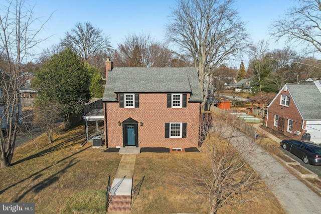 view of front of house featuring brick siding, a chimney, central air condition unit, a shingled roof, and a front lawn