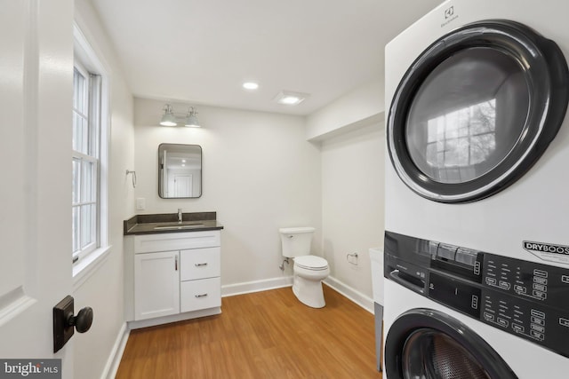 half bath with baseboards, stacked washer and clothes dryer, toilet, wood finished floors, and a healthy amount of sunlight