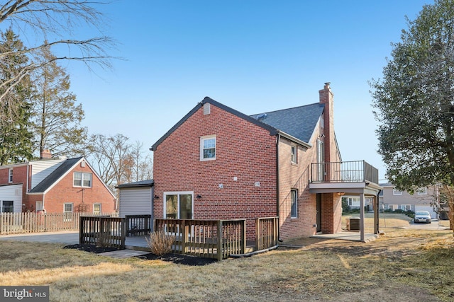 rear view of house with central AC unit, a lawn, a chimney, a deck, and brick siding