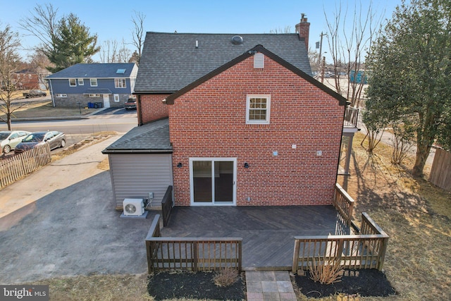 rear view of property with a shingled roof, fence, a deck, and brick siding