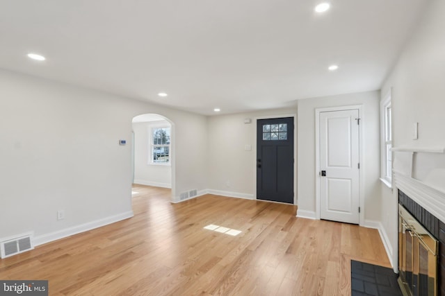 foyer featuring arched walkways, light wood-style flooring, recessed lighting, a fireplace with flush hearth, and visible vents