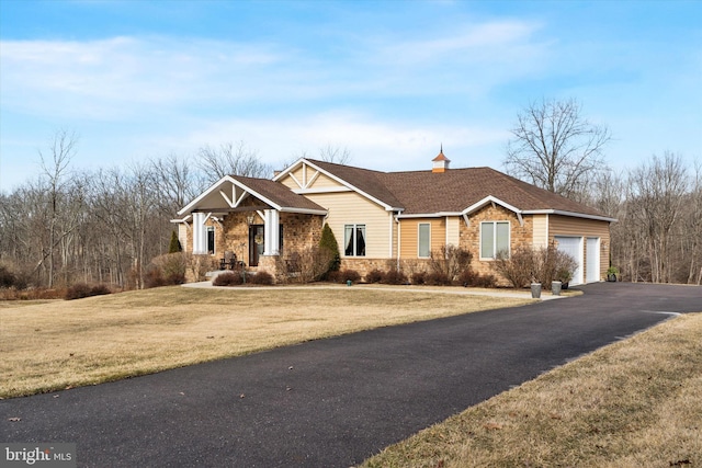 view of front facade featuring an attached garage, stone siding, aphalt driveway, and a front yard