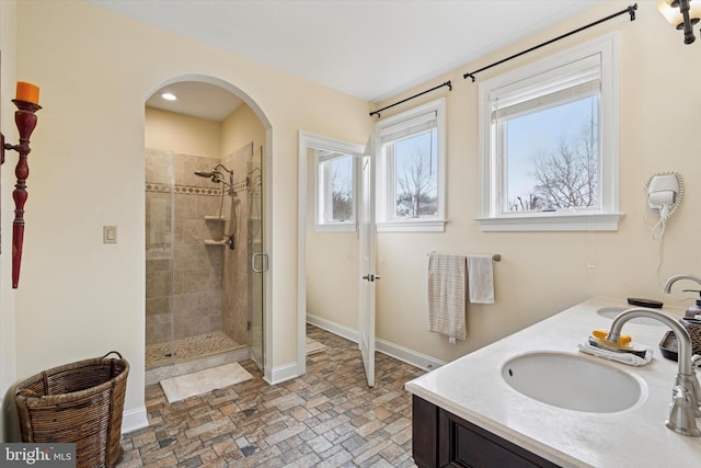 bathroom with a stall shower, a sink, baseboards, and double vanity