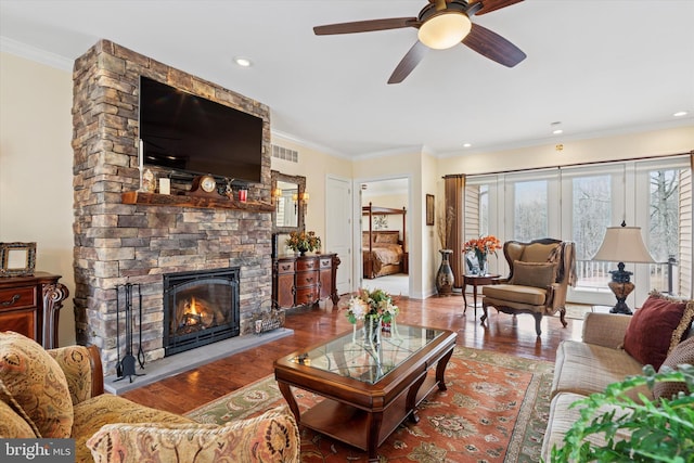 living room featuring ornamental molding, visible vents, a stone fireplace, and wood finished floors