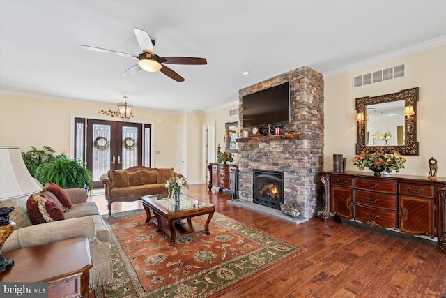 living room featuring crown molding, a fireplace, visible vents, ceiling fan, and wood finished floors