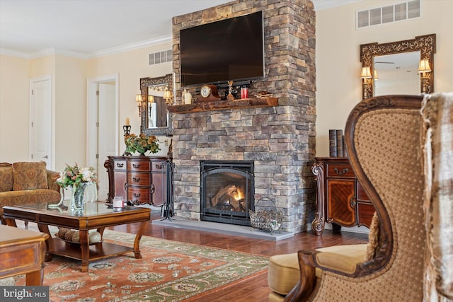 sitting room featuring a stone fireplace, visible vents, crown molding, and wood finished floors