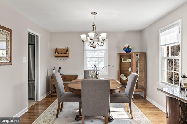 dining space featuring light wood-style floors, baseboards, and an inviting chandelier