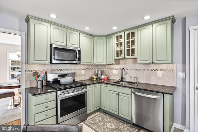 kitchen with dark stone counters, appliances with stainless steel finishes, a sink, and green cabinetry