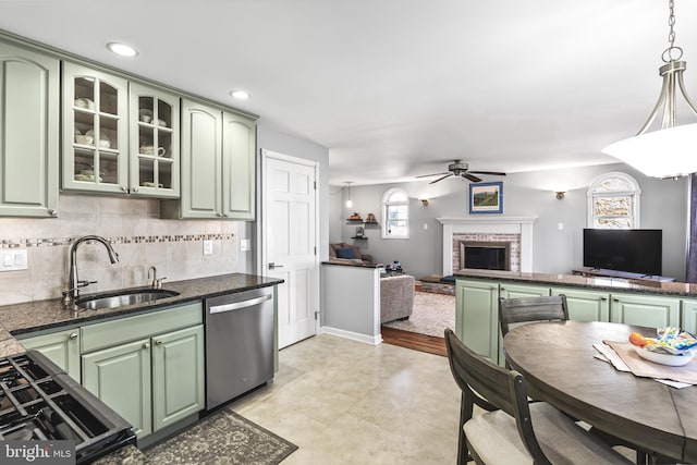 kitchen with stainless steel dishwasher, green cabinets, a brick fireplace, open floor plan, and a sink