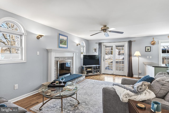 living area with a glass covered fireplace, wood finished floors, a ceiling fan, and baseboards