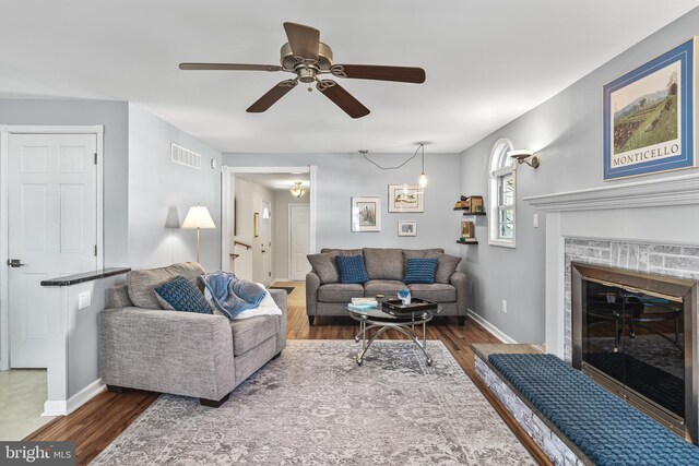 living area with a glass covered fireplace, visible vents, baseboards, and wood finished floors