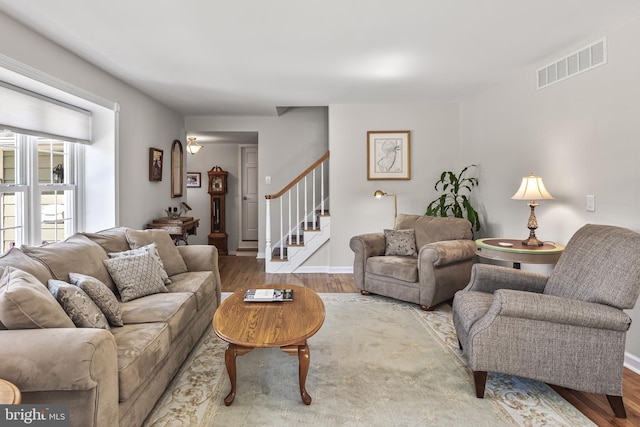 living room featuring stairs, wood finished floors, visible vents, and baseboards