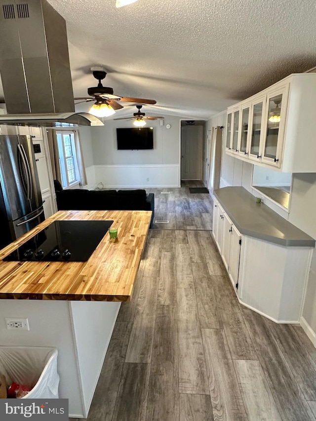 kitchen with freestanding refrigerator, white cabinets, butcher block countertops, black electric cooktop, and exhaust hood