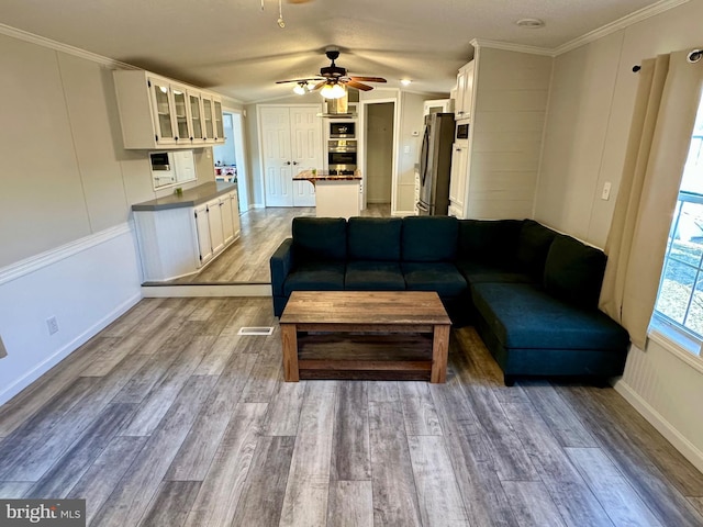 living room with visible vents, a ceiling fan, wood finished floors, vaulted ceiling, and crown molding