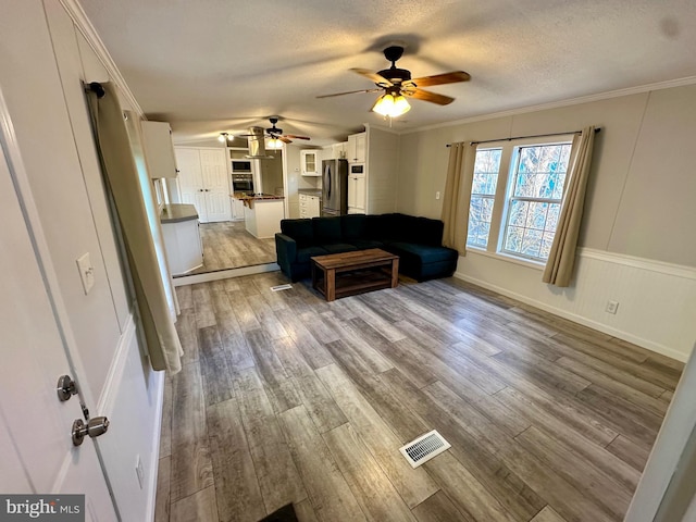 living area with crown molding, visible vents, a ceiling fan, a textured ceiling, and wood finished floors