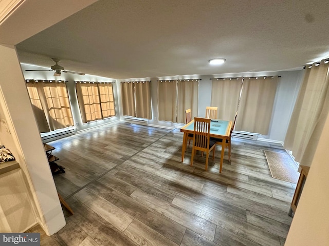 dining area featuring ceiling fan, a baseboard heating unit, a textured ceiling, and wood finished floors