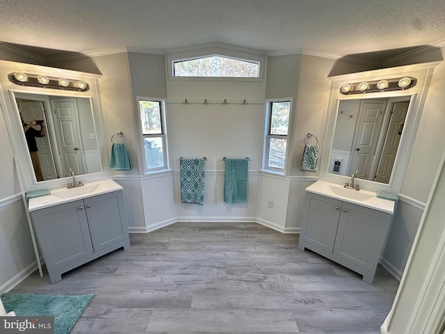 bathroom with a textured ceiling, ornamental molding, two vanities, and a sink