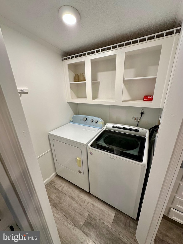 washroom featuring a textured ceiling, laundry area, washing machine and dryer, and light wood-style floors